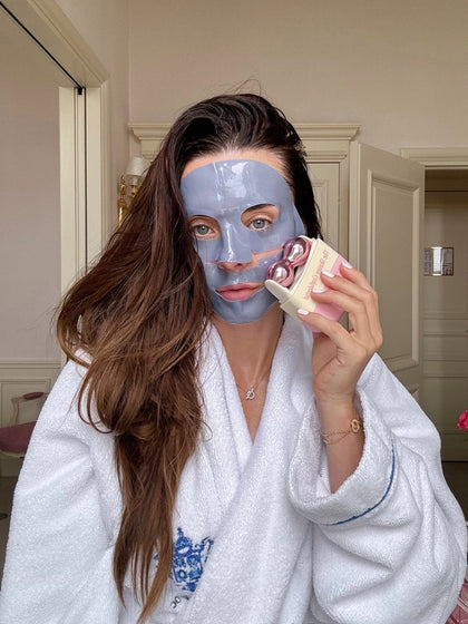 Woman wearing face mask using beauty device in robe. Woman wearing face mask using beauty device in robe.