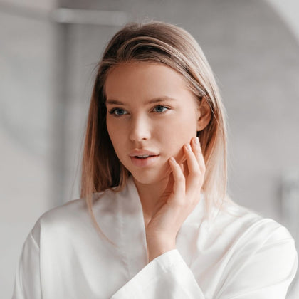 Girl in white robe in bathroom touching face