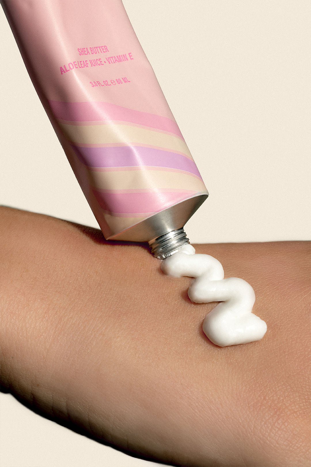 Cream being applied from pink tube onto skin.